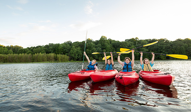Four girls in kayaks posing with their paddles over their heads