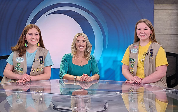 Girl Scouts at a local news station anchor desk with anchor.