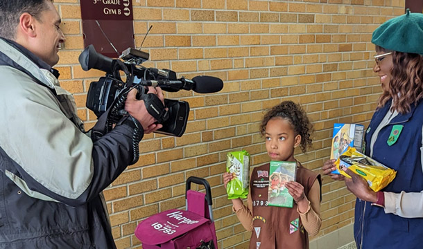 Girl Scouts at a local news station anchor desk with anchor.