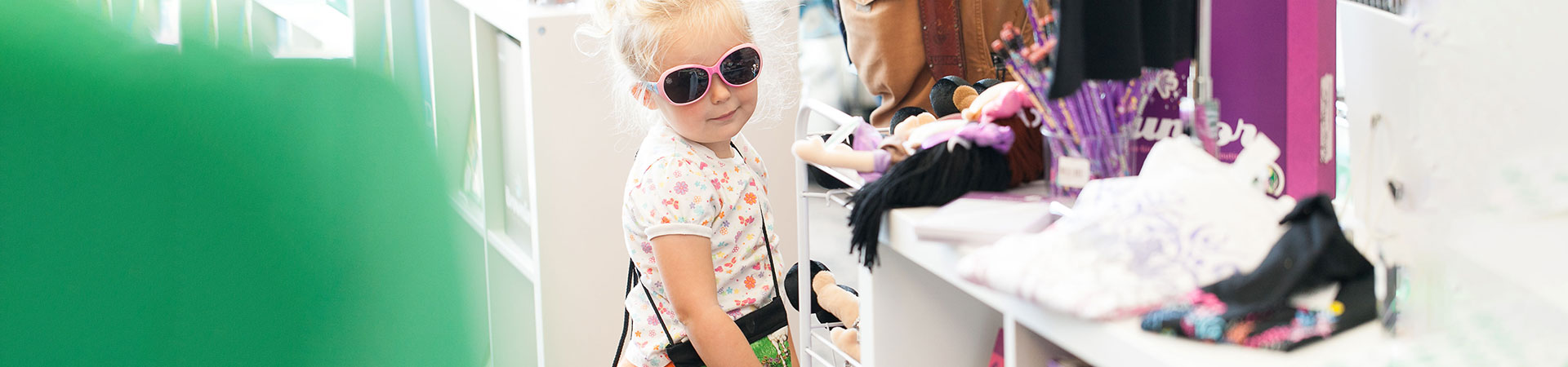  young girl scout trying on pink and blue sunglasses in the shop 