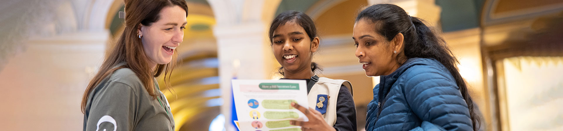  Staff member, Girl Scout and parent looking at list of events at Girl Scout Day at the Capitol 