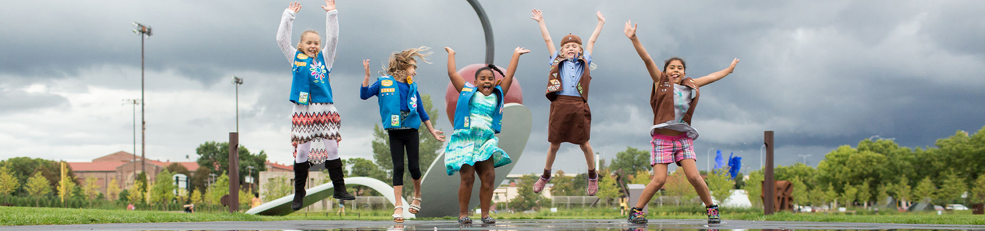  Brownie and Daisy Girl Scouts jumping for a photo in front of the spoon and cherry sculpture at the Minneapolis Sculpture Garden 