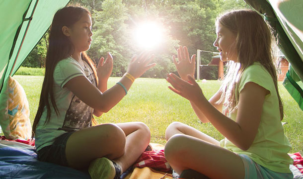 Two girls clapping hands together inside a tent