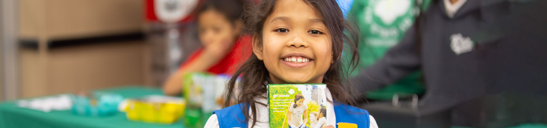  Daisy Girl Scout holding up a box of cookies and smiling 
