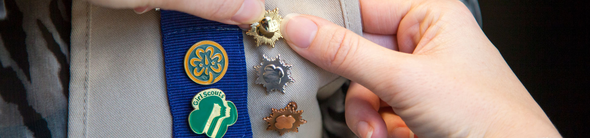  close up of the bronze silver and gold award pins on a Girl Scout vest 